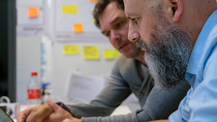 Two men sitting in a conference room have a discussion as they look at a laptop.